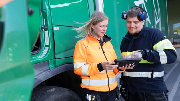 En kvinna och man från Ragn-Sells som står och tittar på en liten handdator framför en grön sopbil