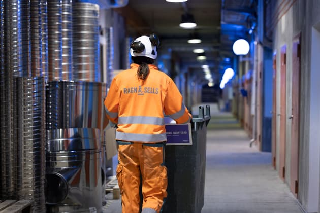 Kvinna från Ragn-Sells bakifrån som drar en avfallsbehållare framför sig i en lång tunnel