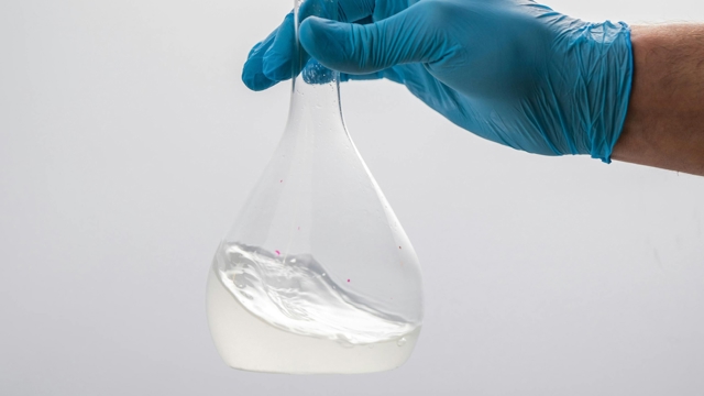 Ett provrör/flaska med en genomskinlig vätska och en hand med en blå handske