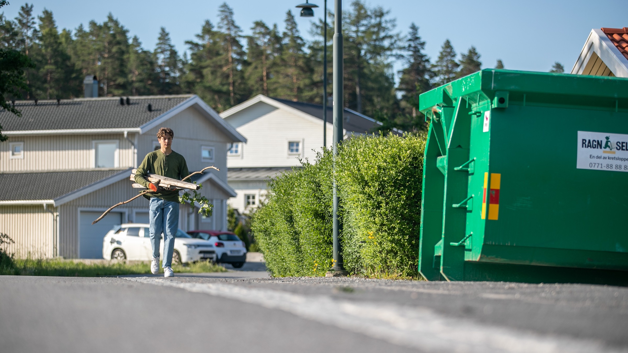 Kille på väg att slänga trä i grön Ragn-Sells container