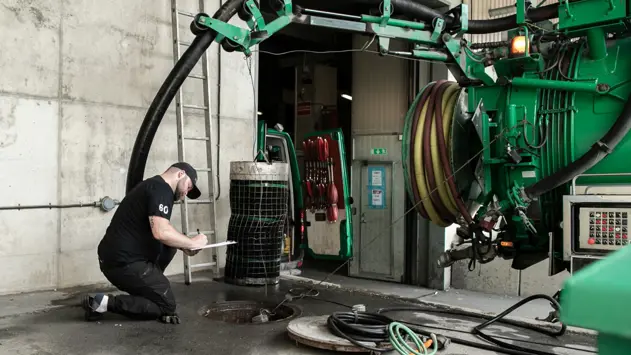 En man från Ragn-Sells står bredvid en oljeavskiljare under marken intill sitt gröna fordon