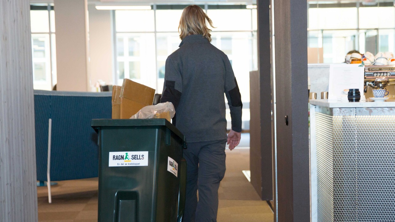 En anställd på Ragn-Sells rullar en behållare med avfall i en fastighet