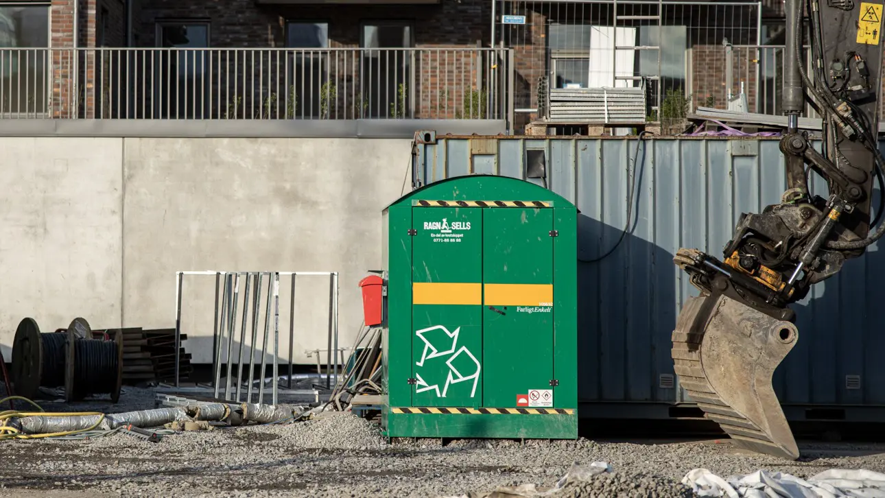 Ett miljöskåp i plåt för förvaring av farligt avfall som står på ett bygge bredvid en grävskopa