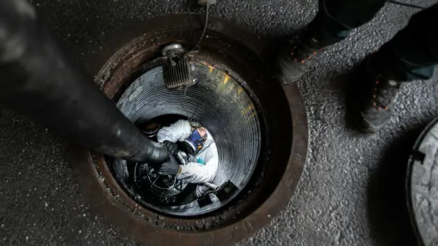 En man med vit overall och ansiktsmask är nere i en oljeavskiljare under marken