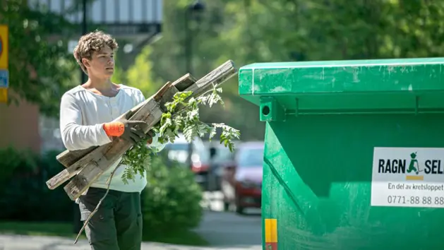 En ung man som slänger träbitar i en grön container