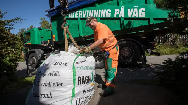 En man fäster en kran i en fylld byggsäck som ska hämtas för återvinning