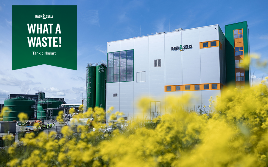 En stor avfallsanläggning i silverfärg med gröna detaljer med gula blommor i förgrunden. Blå himmel och lite moln.